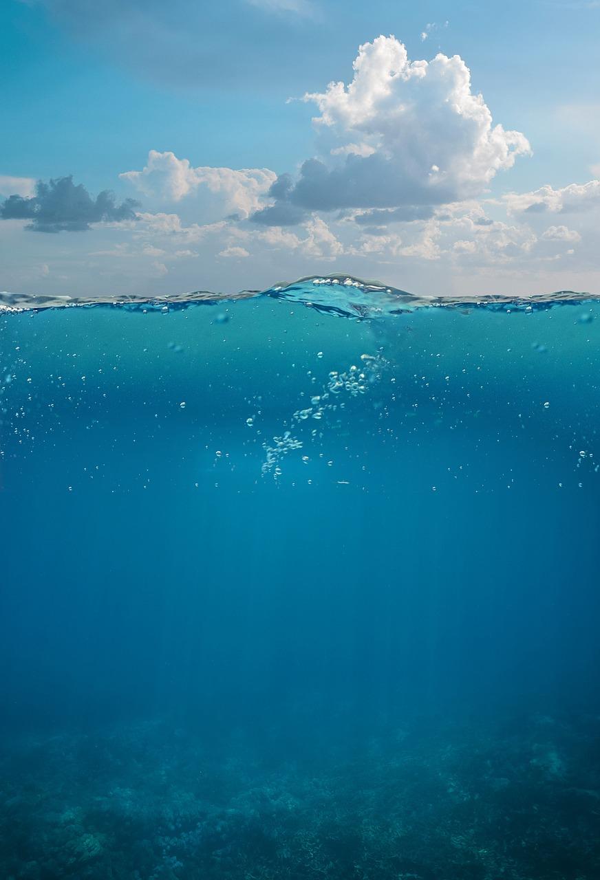 Głębia oceanu, powierzchnia wody, niebo z chmurami i podwodna rafa.