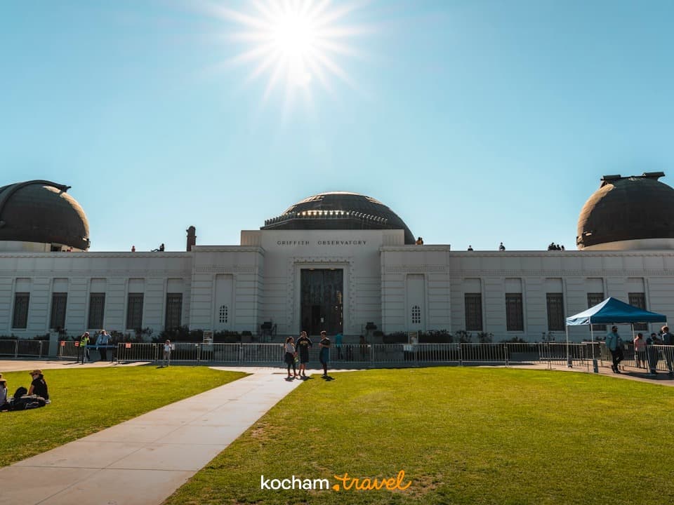 Ikoniczne Obserwatorium Griffitha, Los Angeles, słoneczny dzień, zielony trawnik, turyści.