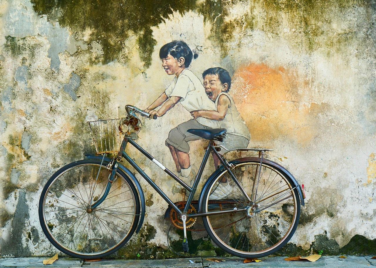 Mural uliczny dzieci na rowerze na starej, omszałej ścianie.