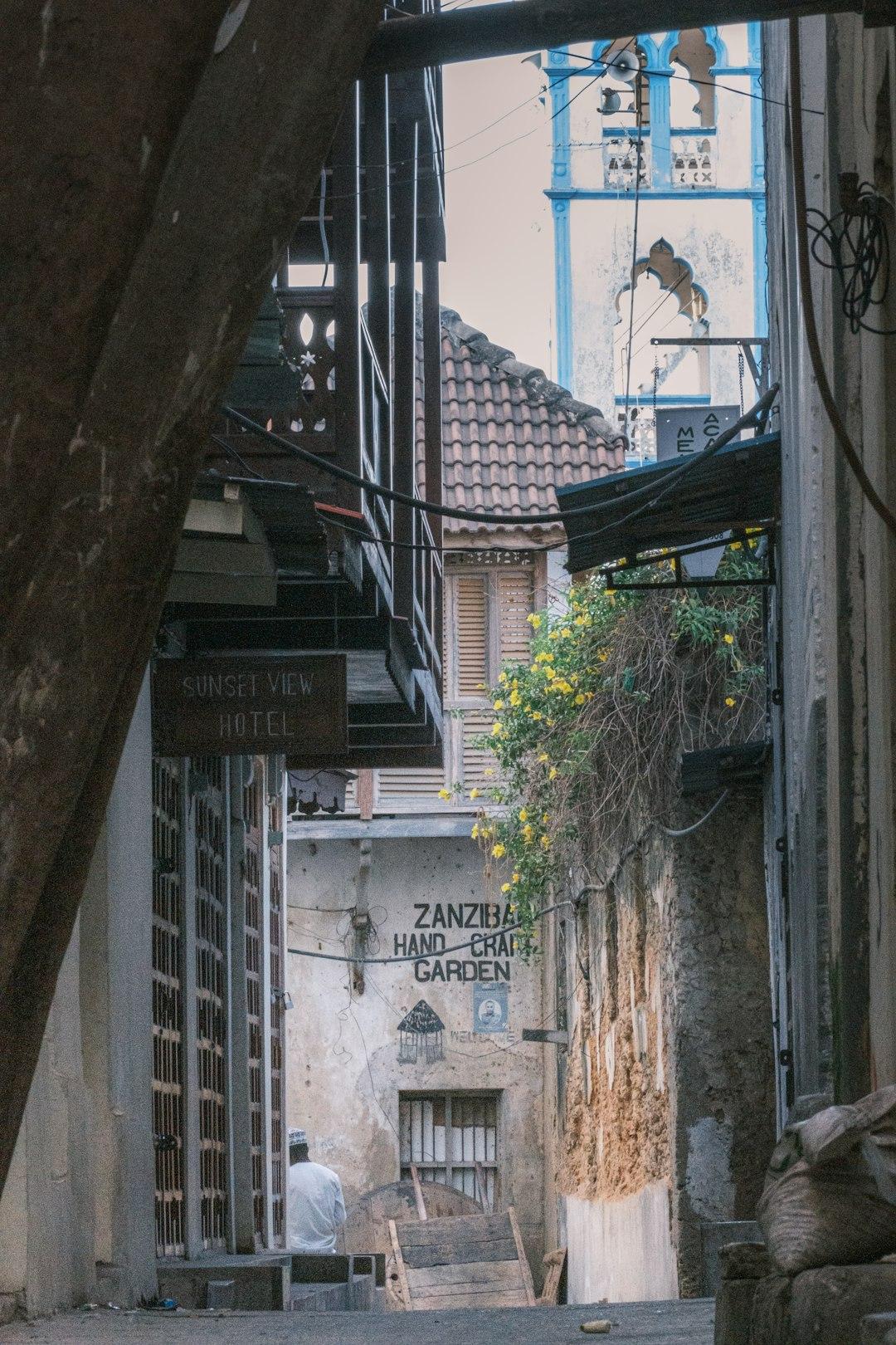 Wąska uliczka Zanzibaru z tradycyjną architekturą, minaretem i siedzącym mężczyzną.