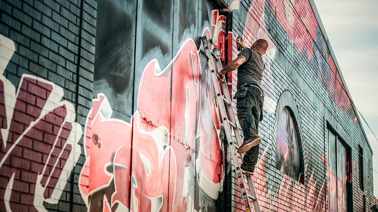 Artysta malujący kolorowe graffiti na ceglanej ścianie miejskiego budynku.