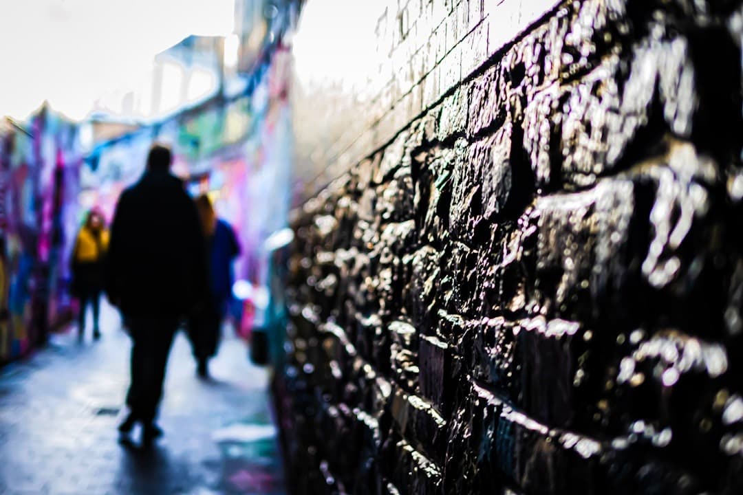 Wąska, ciemna uliczka z graffiti, teksturą kamiennej ściany i rozmyci ludzie.