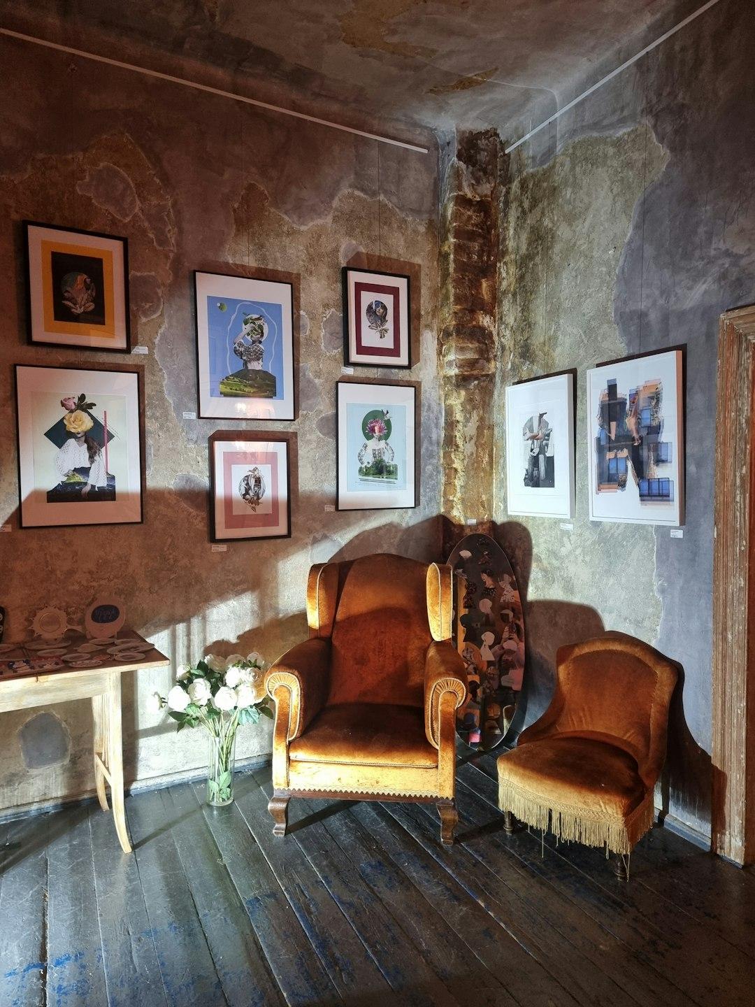 Ekspozycja sztuki w galerii z vintage fotelami i zniszczonymi ścianami.