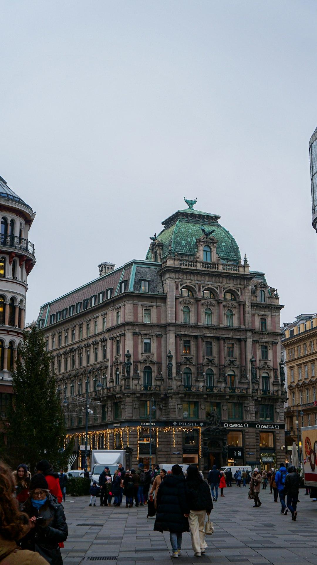 Zabytkowy budynek z zieloną kopułą, piesi na ulicy, świąteczne światła.