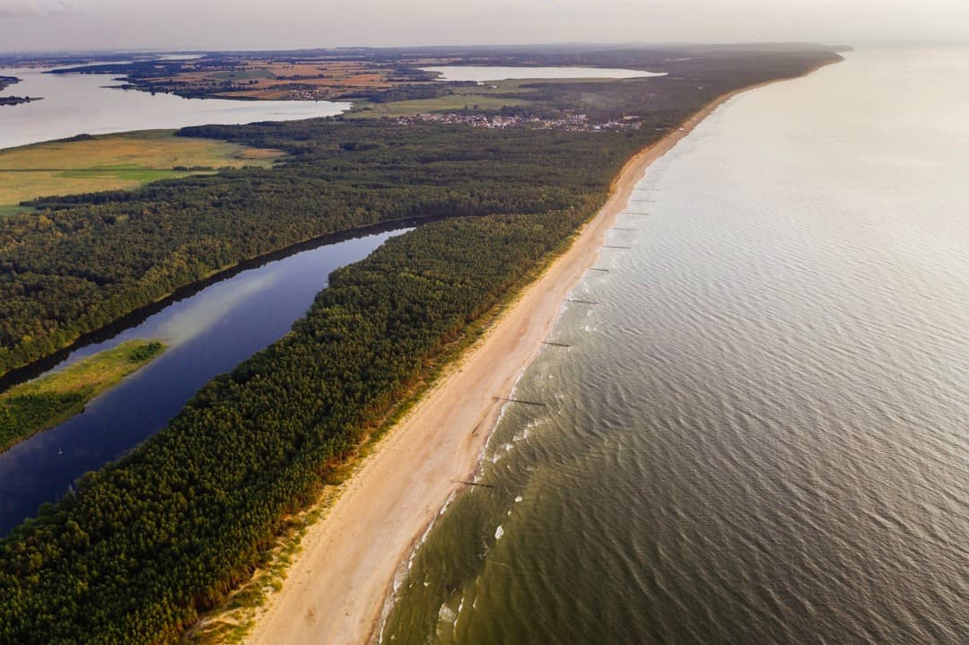 Panoramiczny widok wybrzeża: piaszczysta plaża, las i rzeka.