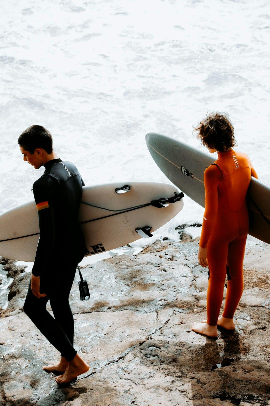 Dwóch surferów w piankach z deskami surfingowymi na skalistym wybrzeżu.