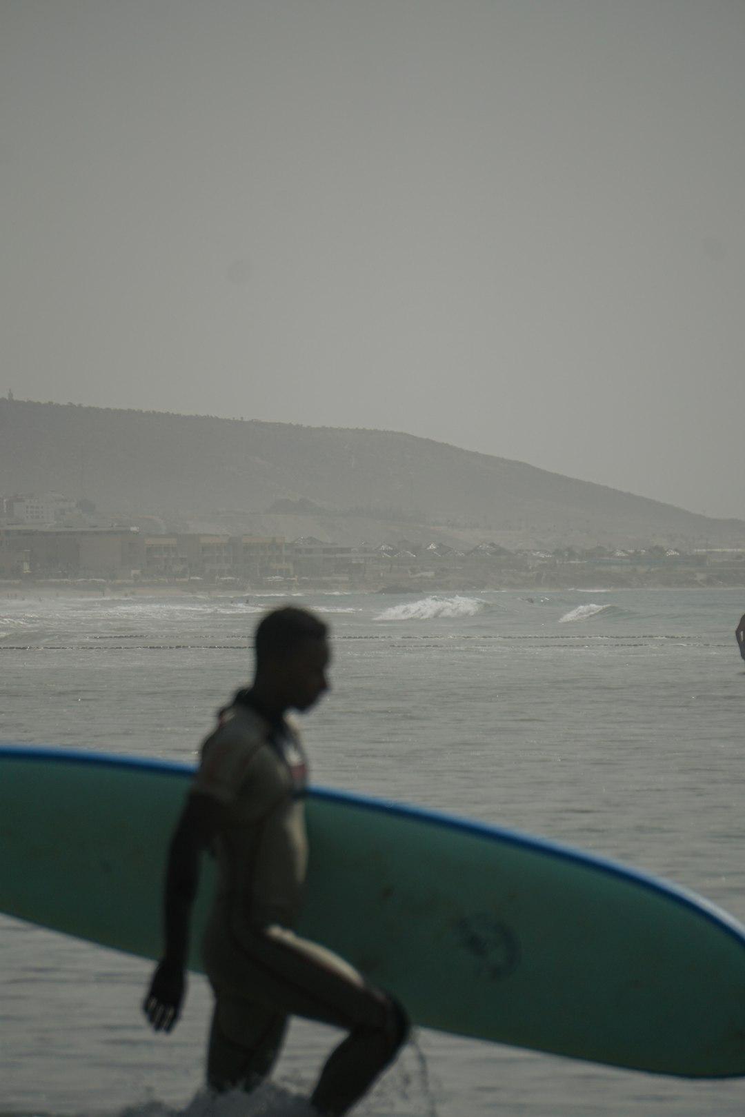 Surfer w kombinezonie niosący deskę surfingową w oceanie.