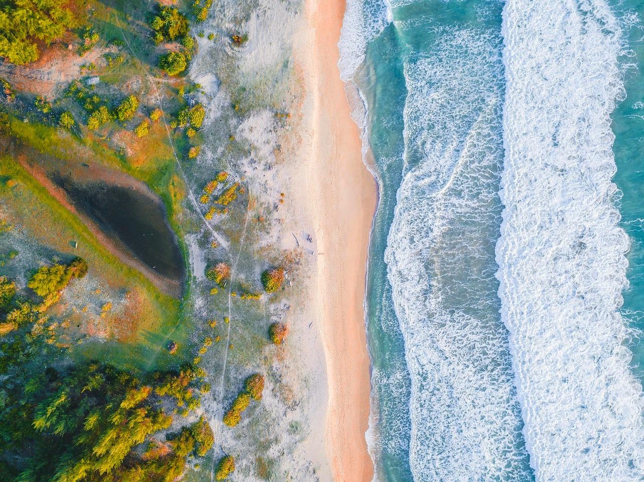 Widok z lotu ptaka: piaszczysta plaża, turkusowe fale, zielone wybrzeże, laguna.