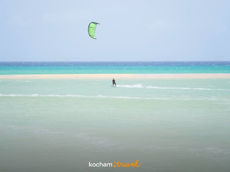 Kitesurfer na turkusowej wodzie, piaszczysta ławica, błękitny ocean, słoneczny dzień.