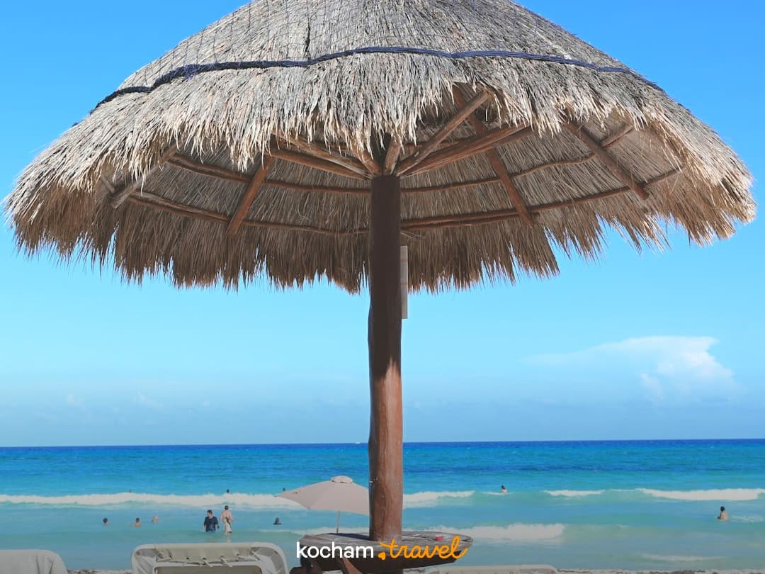 Słomiany parasol palapa na piaszczystej plaży, turkusowe morze.