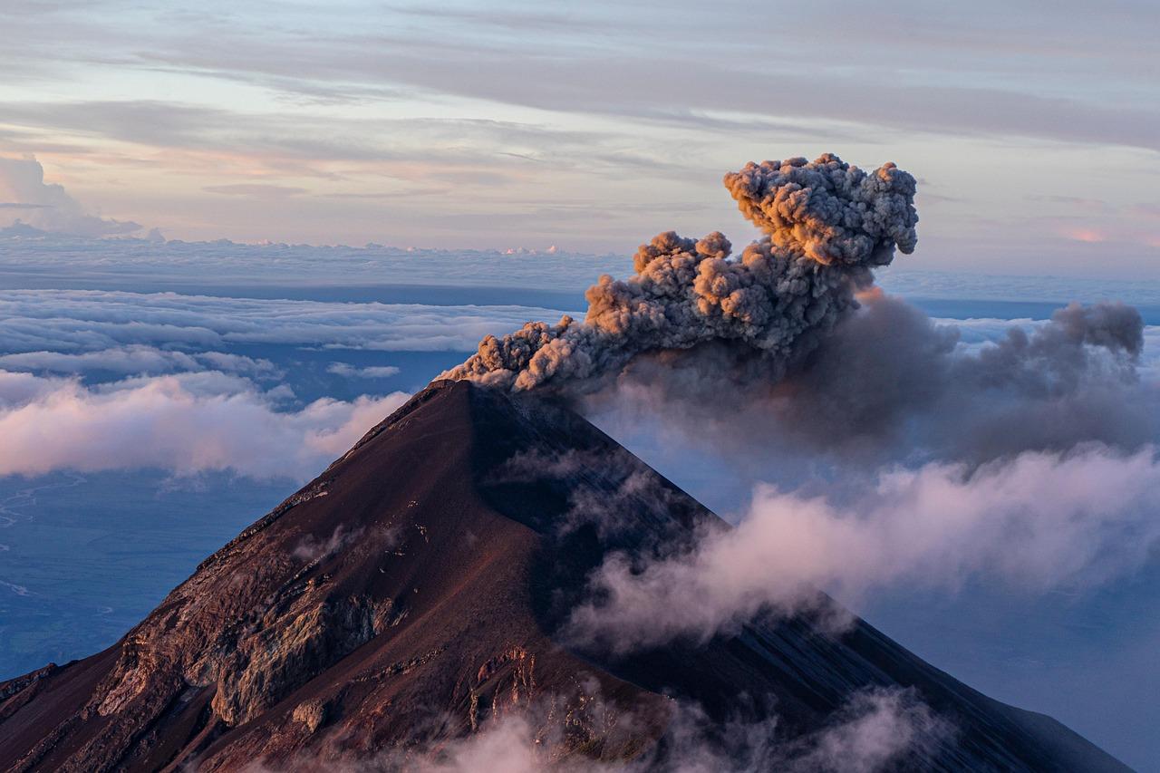 Potężna erupcja wulkanu z pióropuszem popiołu o wschodzie słońca nad chmurami.