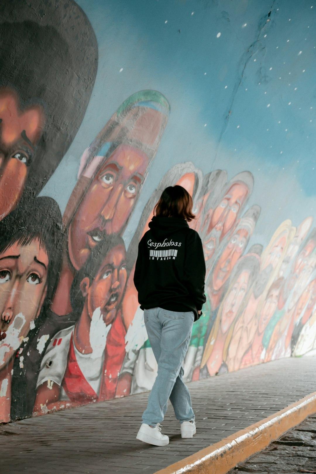 Młoda osoba idąca tunelem z kolorowymi muralami i gwiaździstym sufitem.