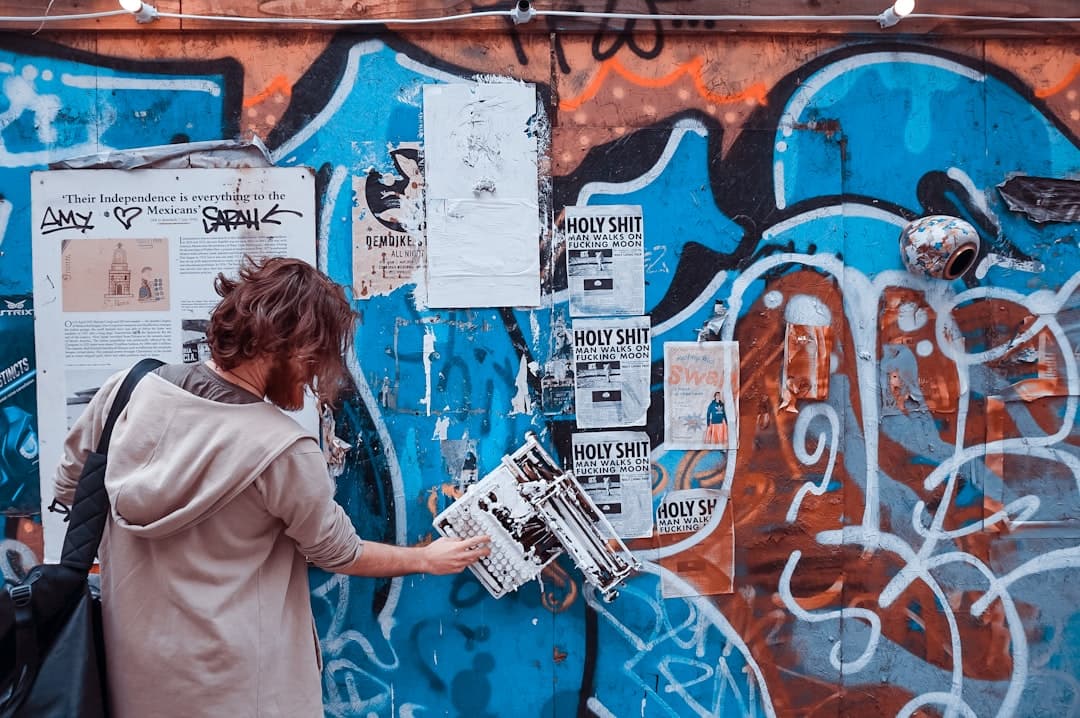Człowiek mocujący poplamioną farbą maszynę do pisania na ścianie z graffiti.