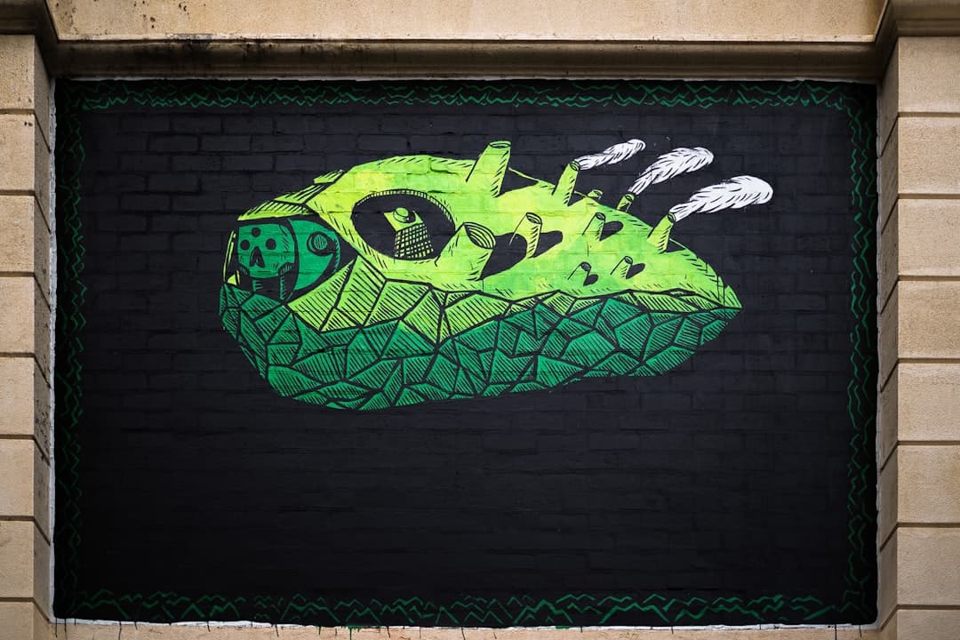 Zielony mural przemysłowy z kominami i czaszką na ceglanej ścianie.