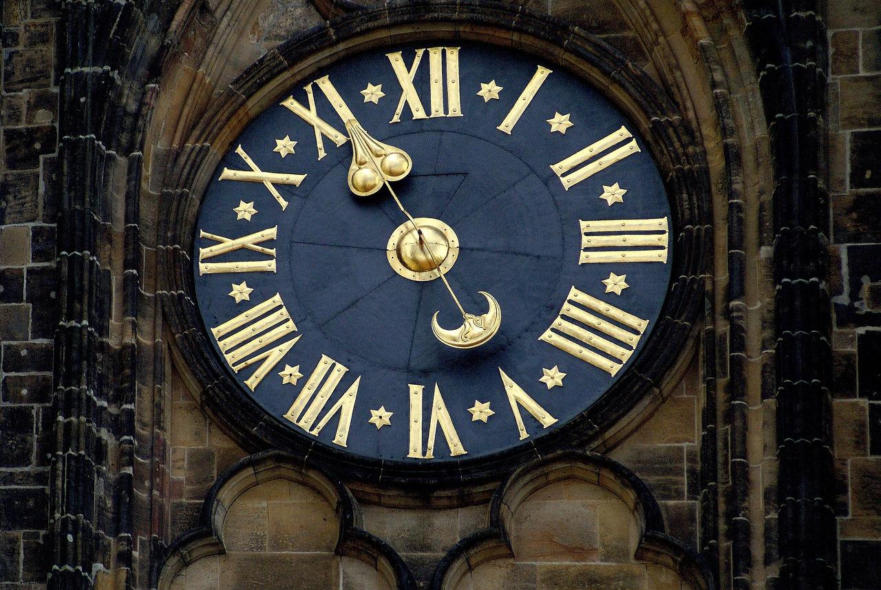 Ozdobny zegar astronomiczny ze złotymi cyframi rzymskimi na kamiennej wieży.
