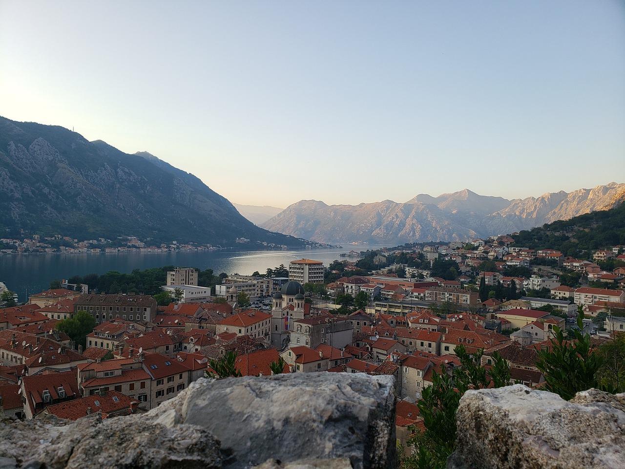 Panorama miasta Kotor z czerwonymi dachami nad zatoką i górami.