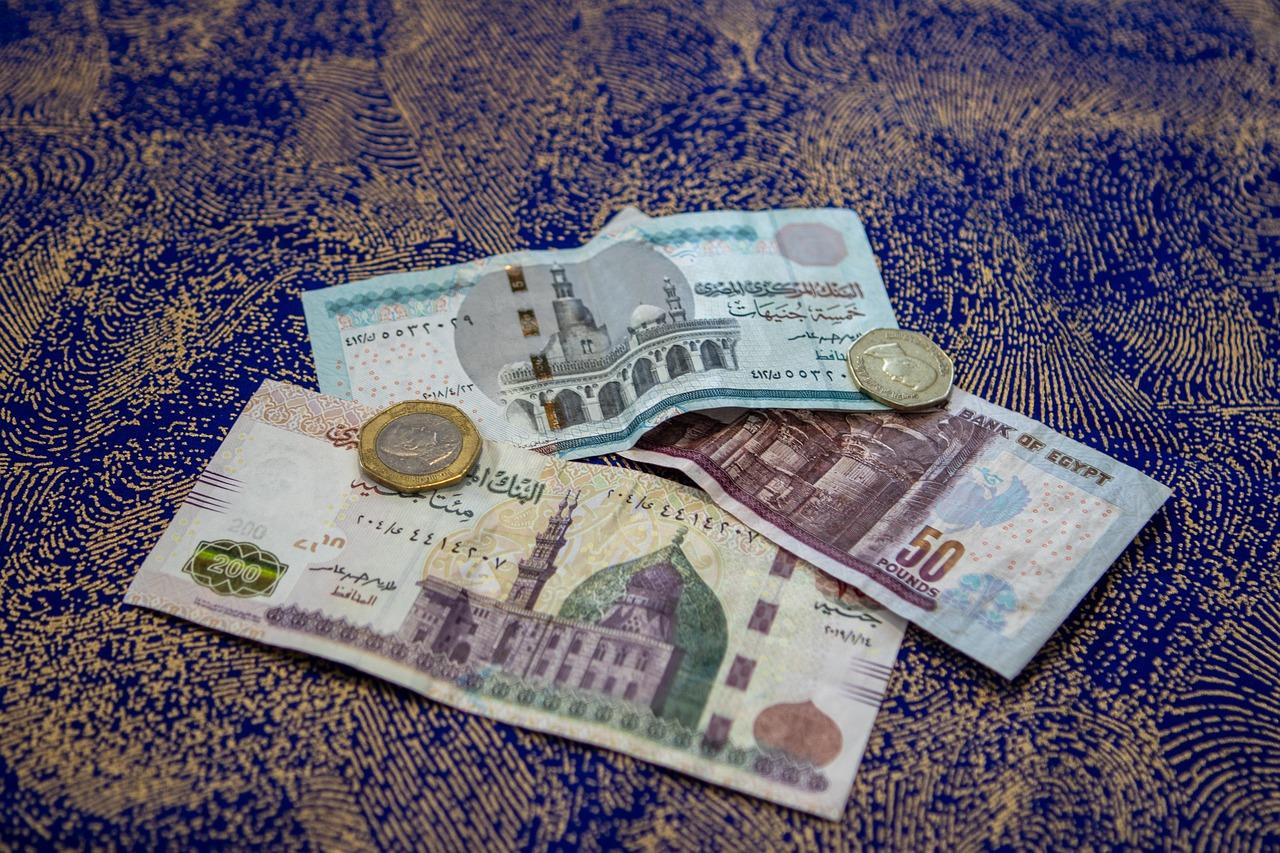 Egipskie funty, banknoty i monety, na ozdobnym niebieskim materiale.