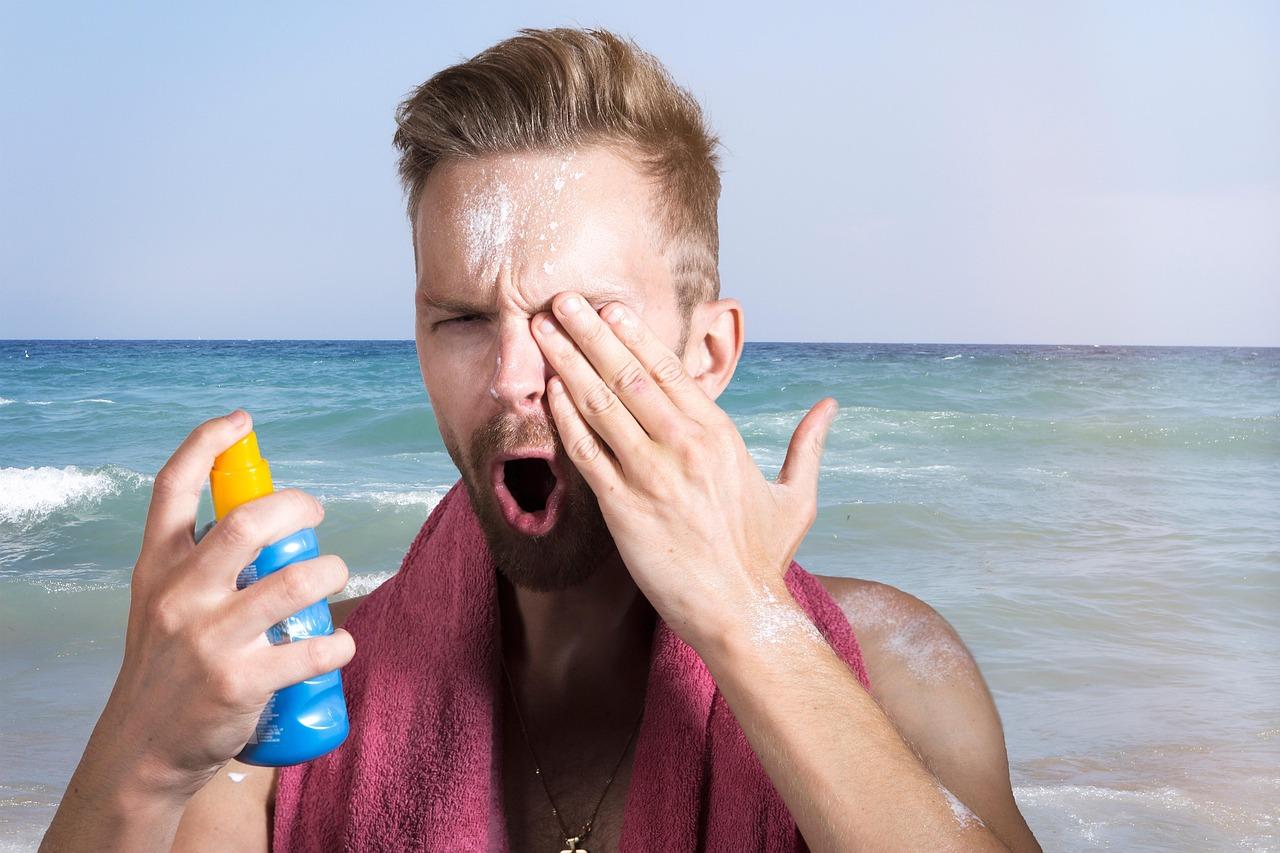 Mężczyzna na plaży z kremem przeciwsłonecznym w oku, trzymający butelkę sprayu.