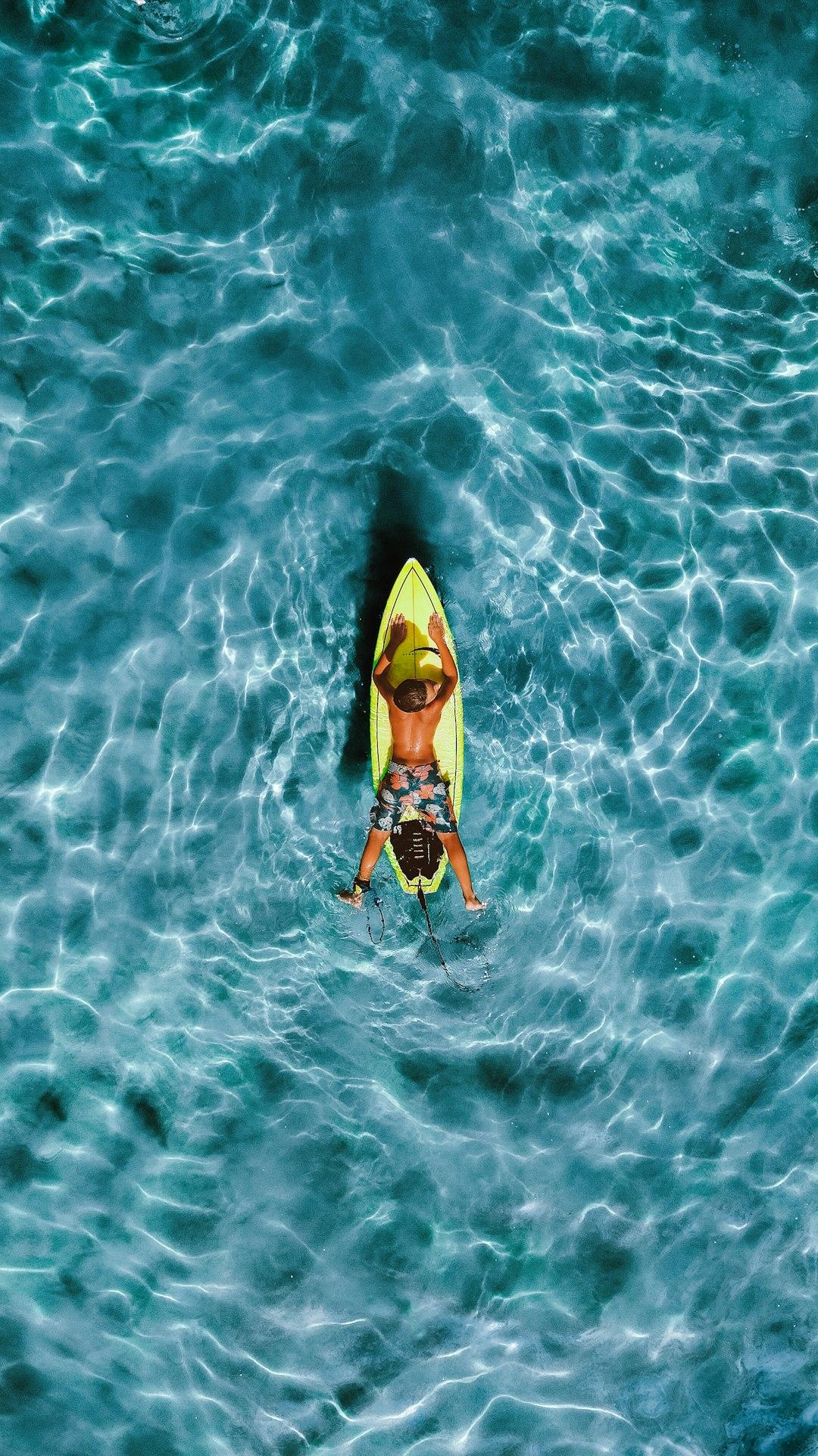 Młody surfer leżący na żółtej desce surfingowej w turkusowej wodzie.