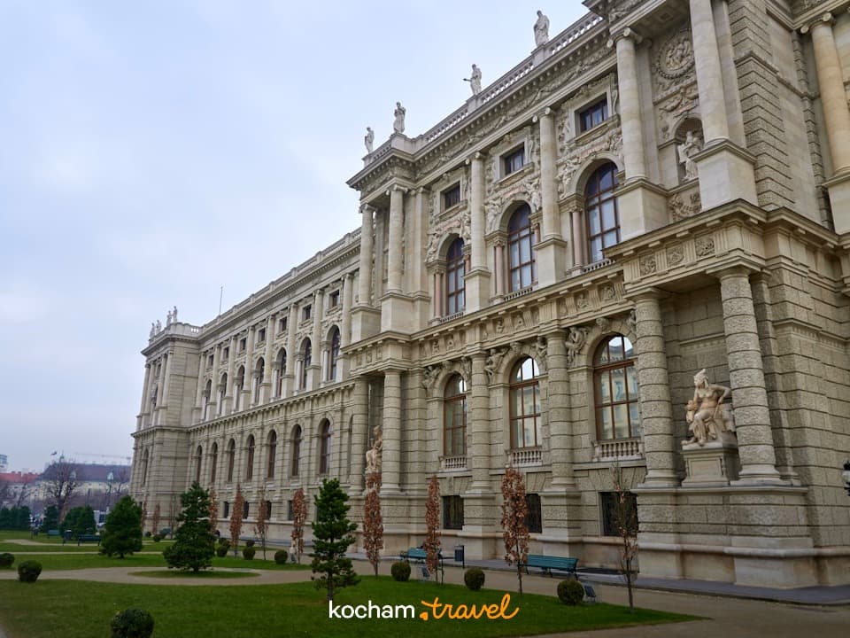 Zdobiony historyczny budynek, klasyczna architektura, zielony park, pochmurny dzień.
