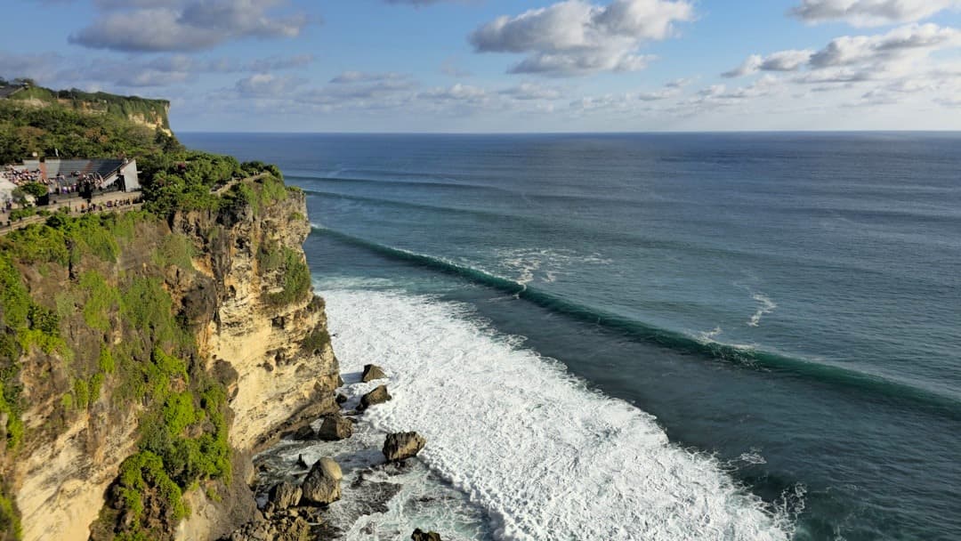 Klif z zielenią, błękitny ocean, fale, świątynia Bali.