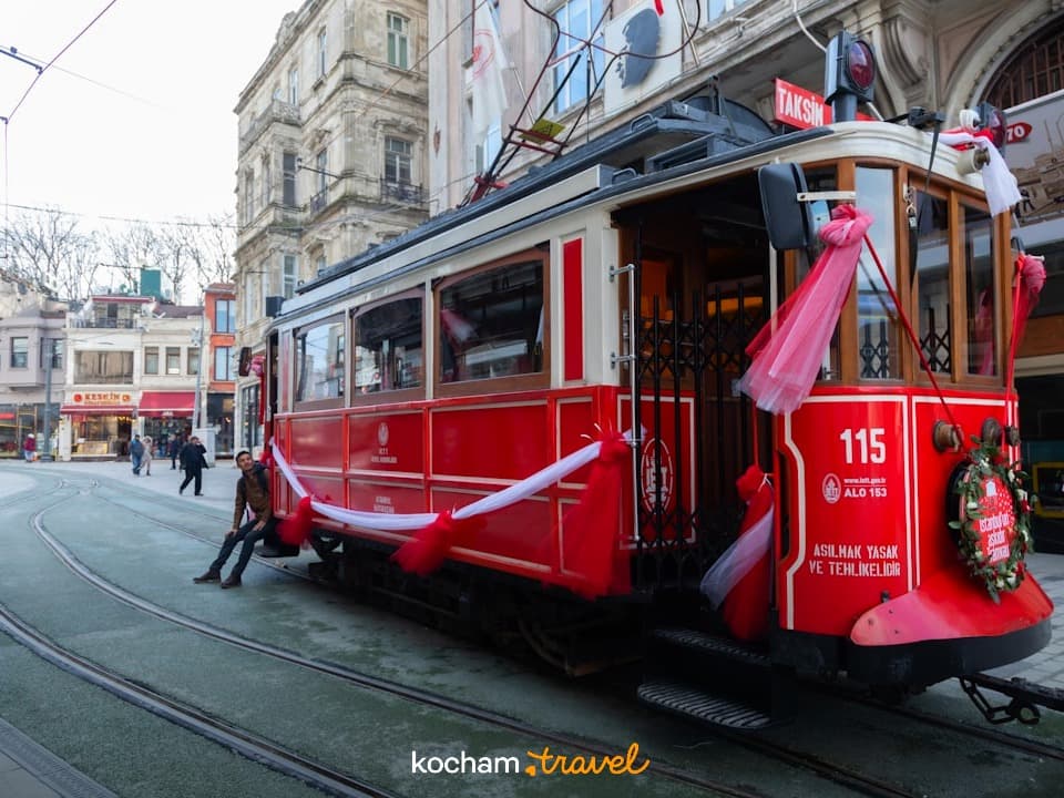 Historyczny czerwony tramwaj z ozdobami i mężczyzną na ulicy.
