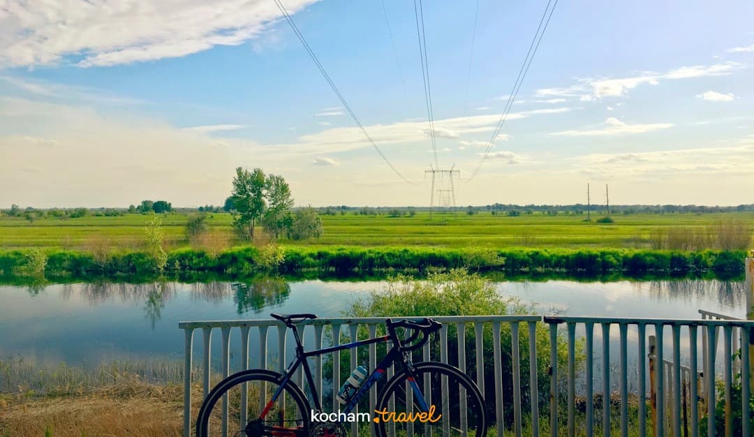 Rower przy balustradzie, rzeka, zielone pola, słoneczny dzień.