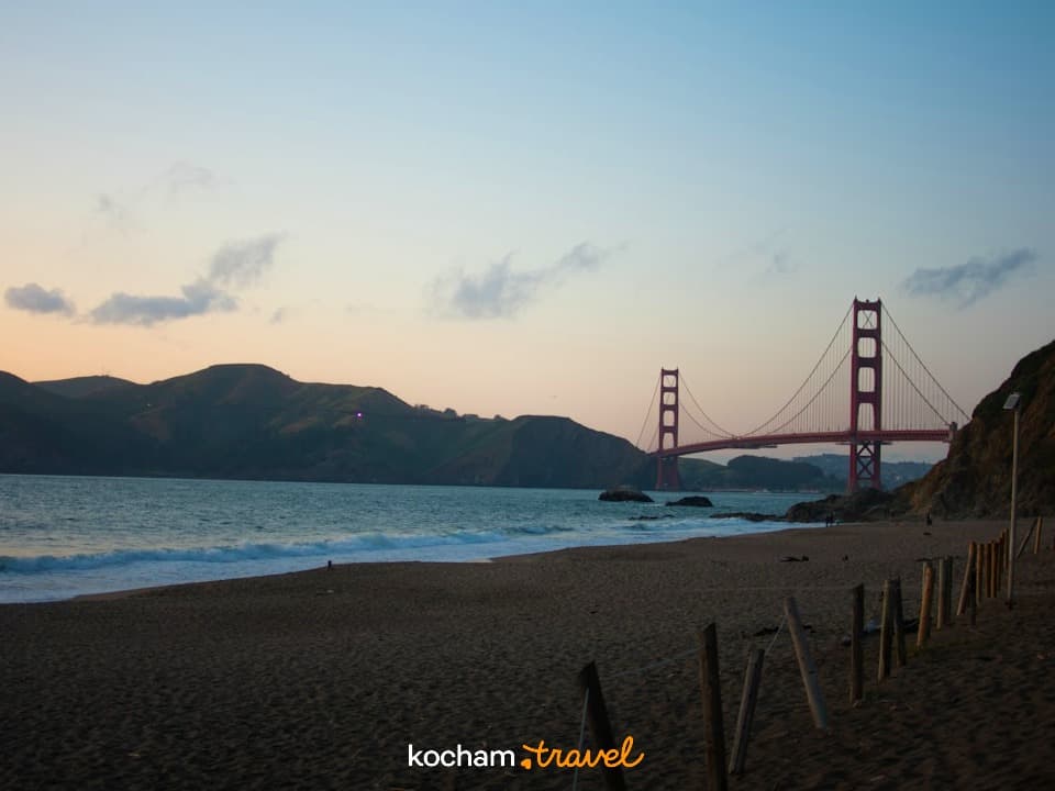 Ikoniczny Most Golden Gate z piaszczystej plaży o zmierzchu.