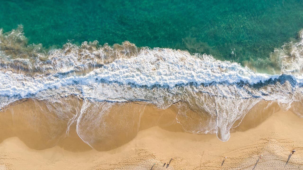 Turkusowe fale oceanu rozbijające się o złotą plażę z lotu ptaka.