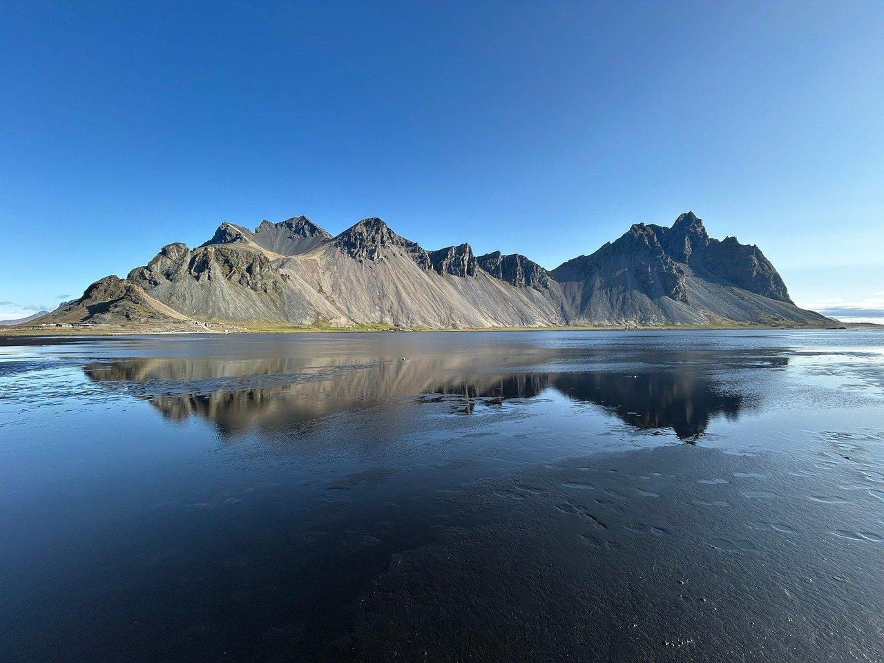 Góry Vestrahorn odbijające się w wodzie na czarnej plaży Islandii.