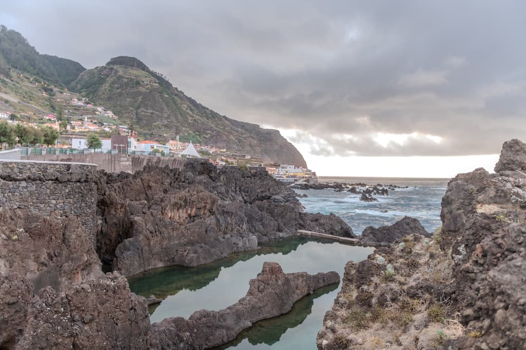Naturalne baseny wulkaniczne Porto Moniz z miasteczkiem na zielonym wzgórzu.