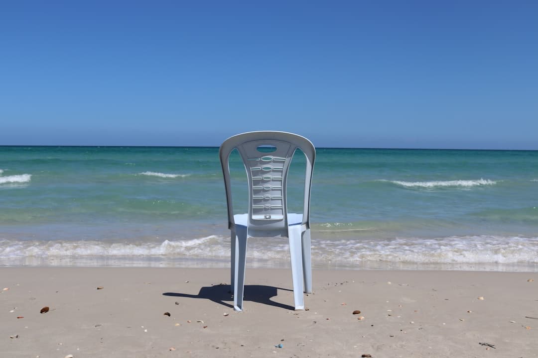 Białe plastikowe krzesło na piaszczystej plaży z turkusowym morzem i błękitnym niebem.