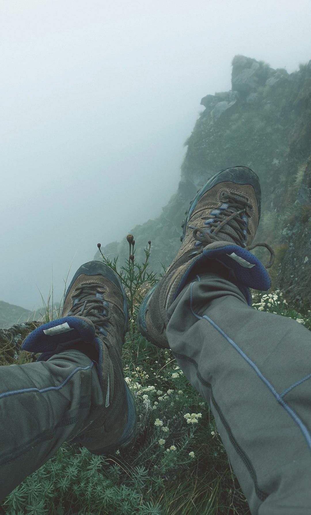 Buty trekkingowe i nogi na skalistym zboczu, mgliste góry.
