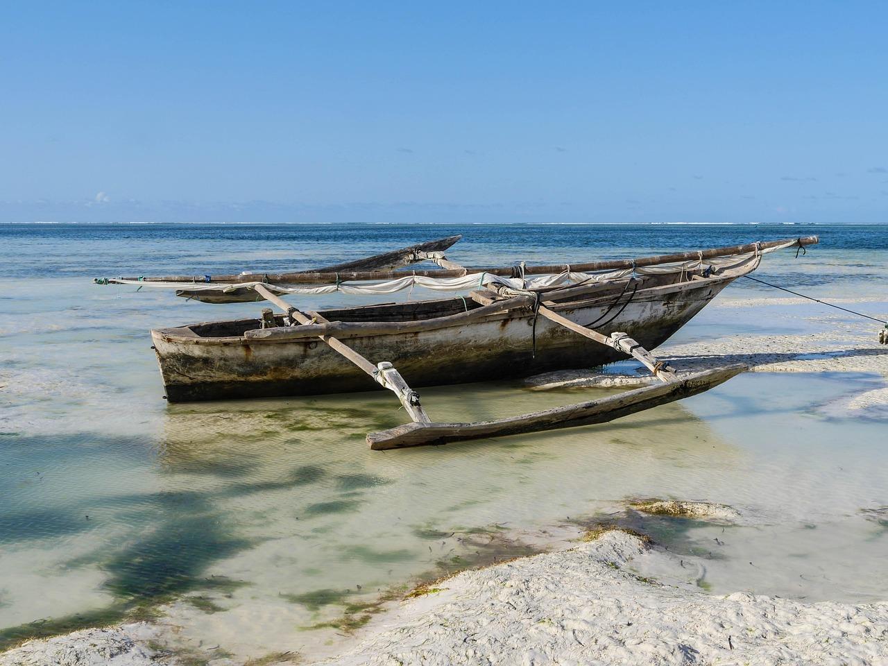 Dwie tradycyjne łodzie z pływakami w płytkiej wodzie przy tropikalnej plaży.