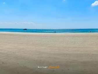 Szeroka piaszczysta plaża z turkusową wodą i błękitnym niebem.