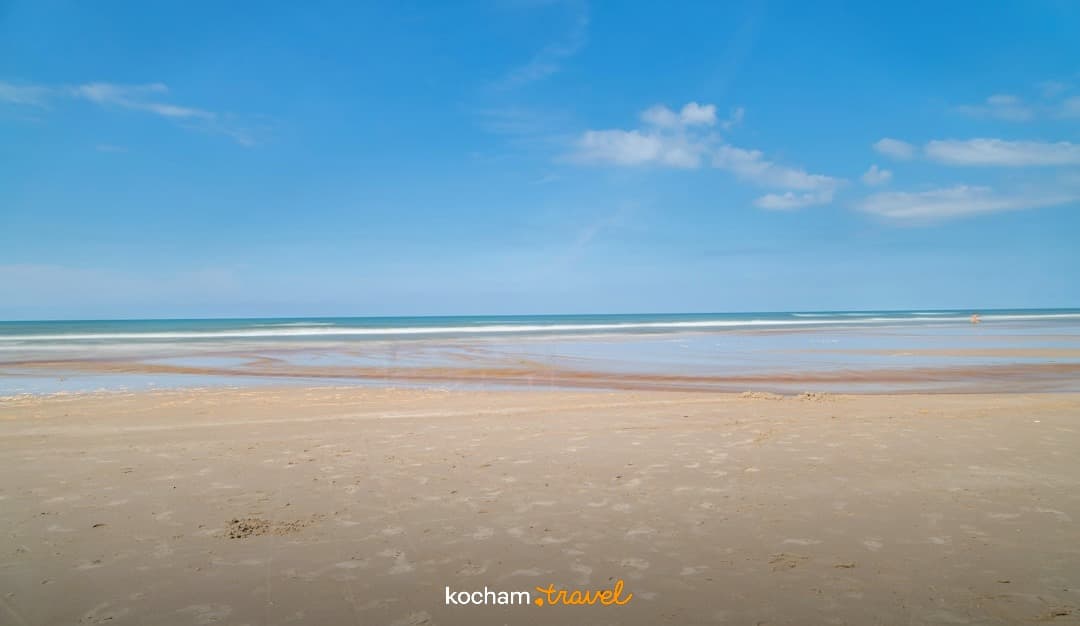 Szeroka piaszczysta plaża, ocean, błękitne niebo, spokojne fale.