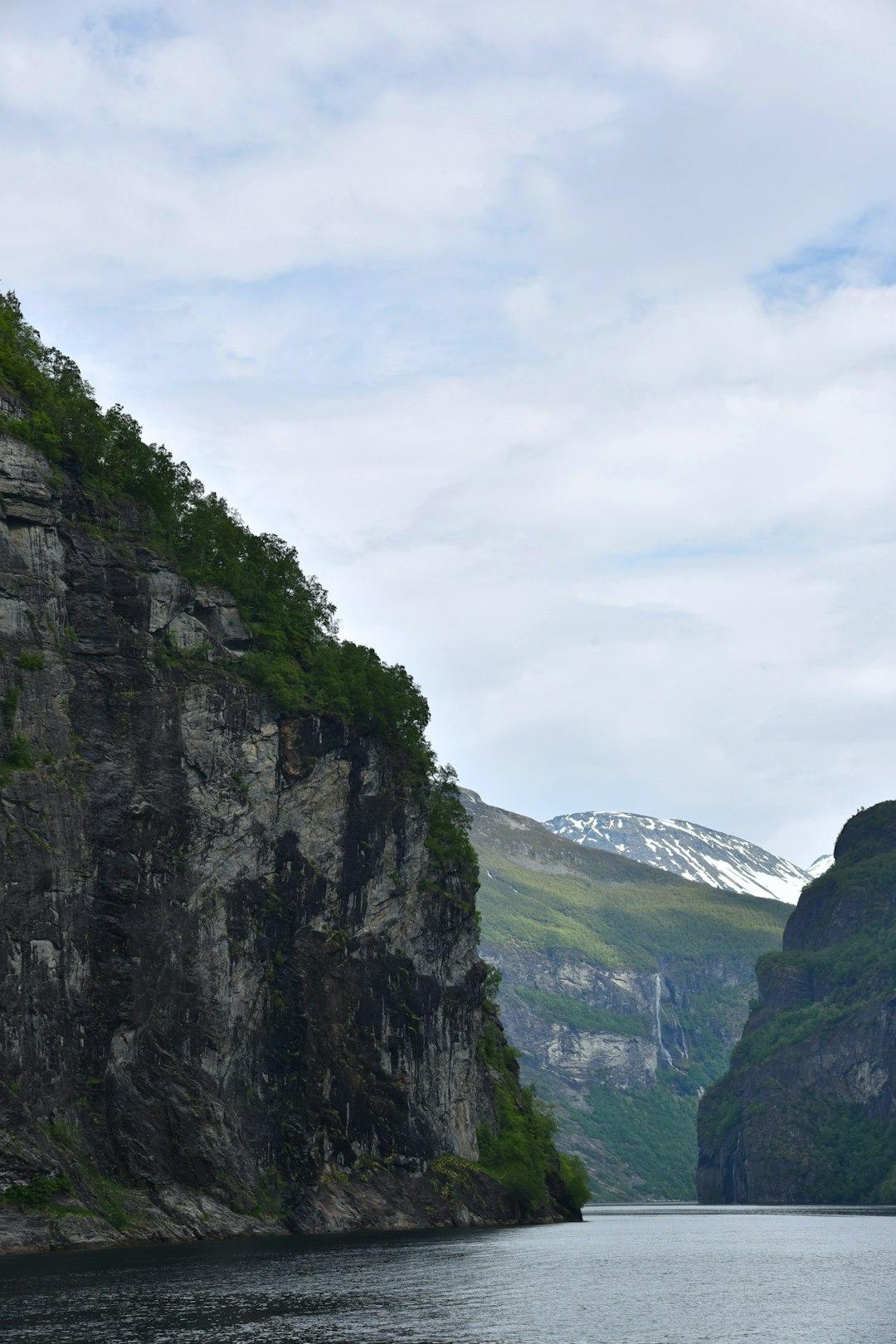 Malowniczy fiord norweski: skaliste klify, zalesione zbocza, wodospad, ośnieżone szczyty.