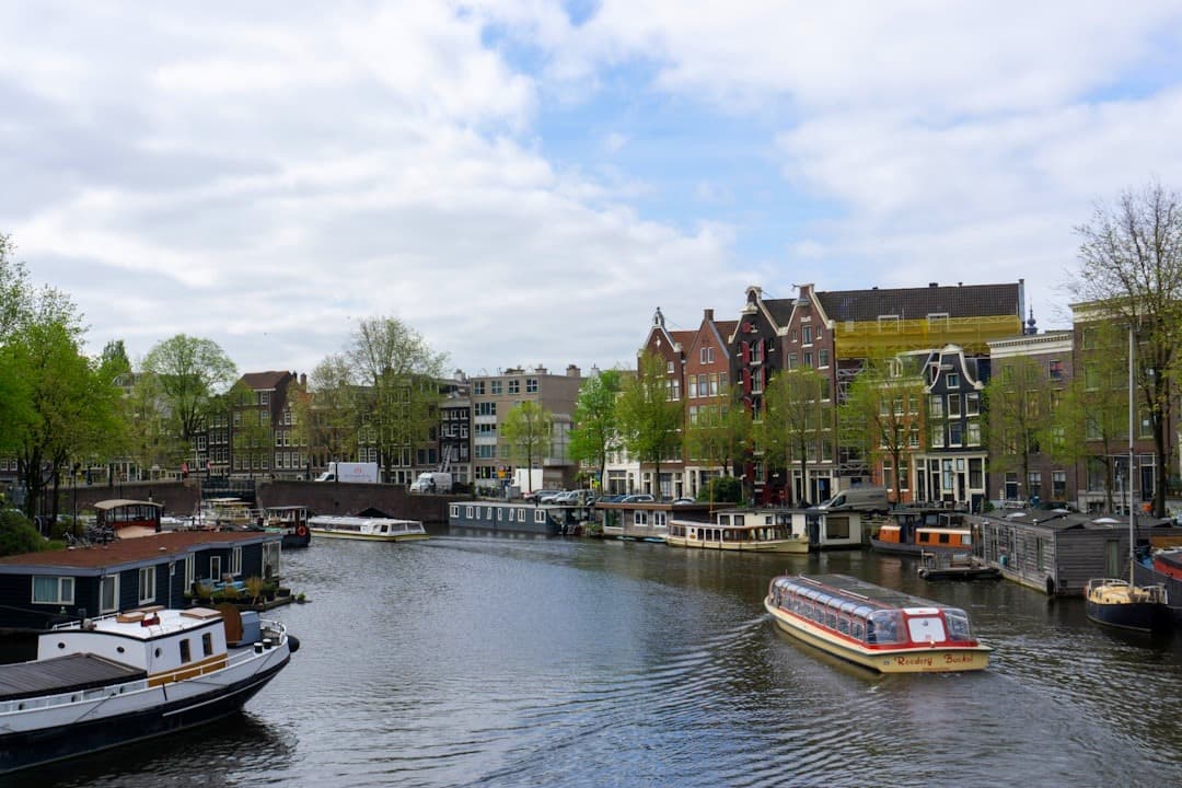 Malowniczy kanał w Amsterdamie, zabytkowe kamienice, łodzie mieszkalne, statek wycieczkowy.