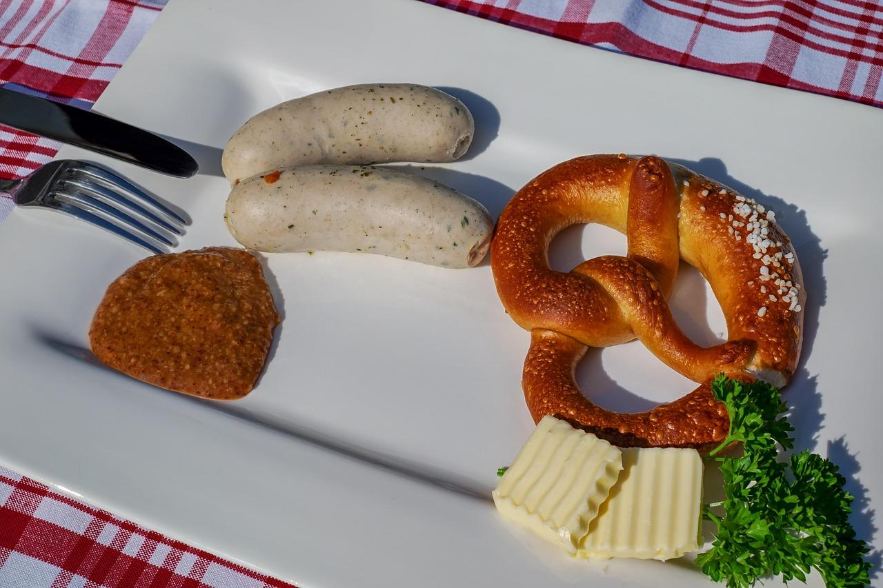 Bawarskie białe kiełbaski Weisswurst, precel, musztarda i masło na talerzu.