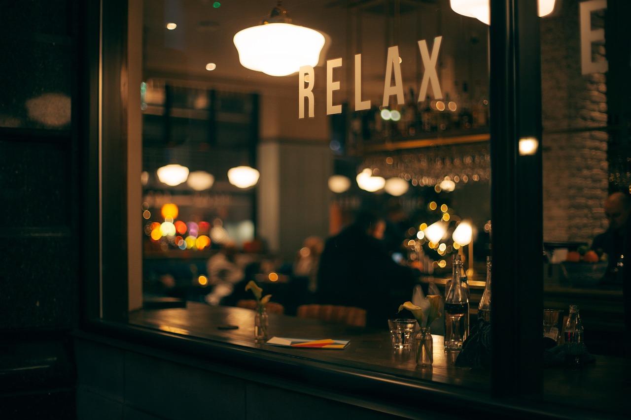 Wnętrze baru lub restauracji widziane przez okno nocą, napis RELAX.