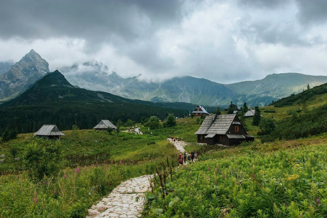 Górska dolina z drewnianymi chatami i turystami na szlaku.