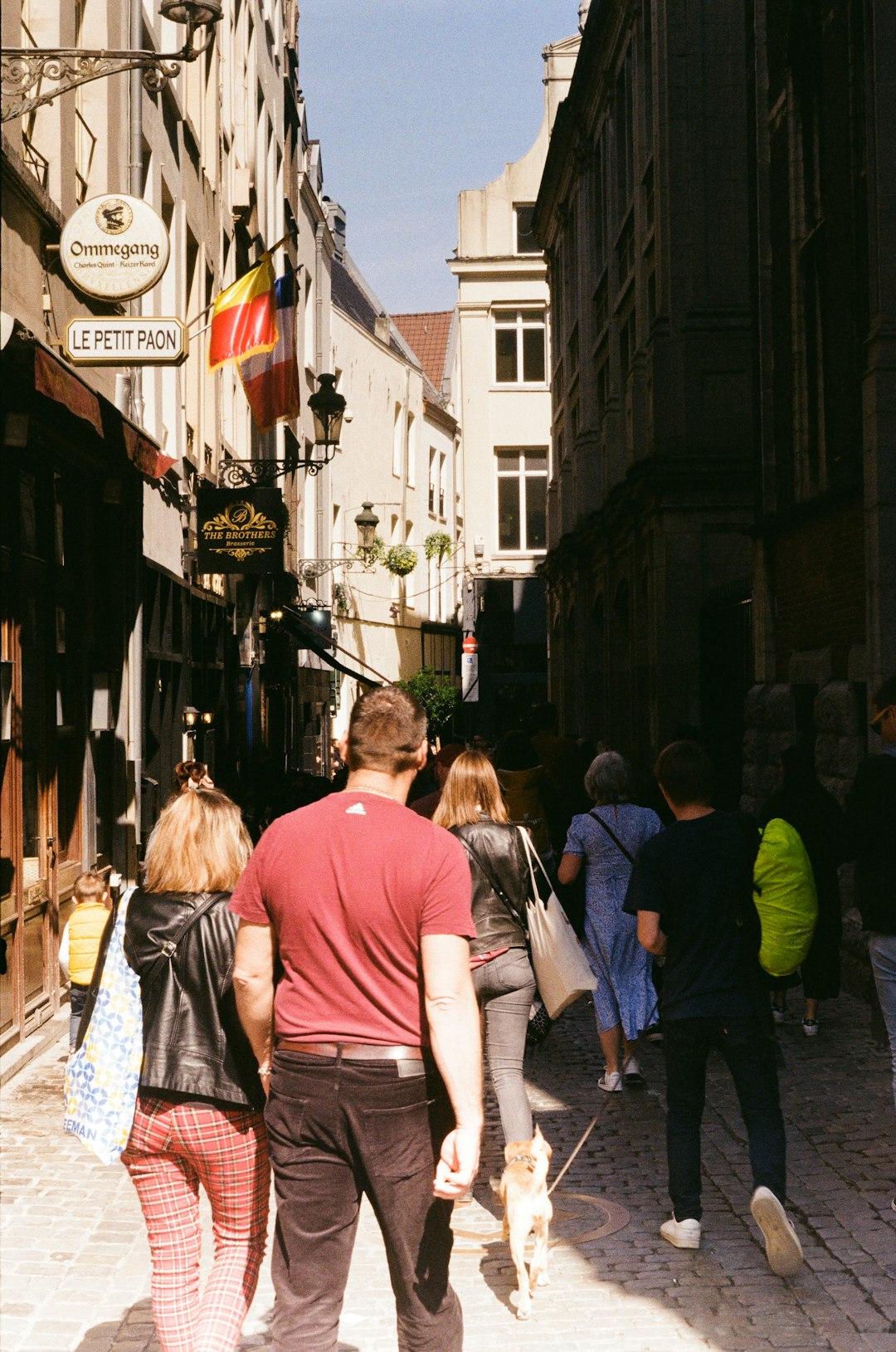 Ludzie spacerujący brukowaną ulicą między zabytkowymi budynkami w słońcu.