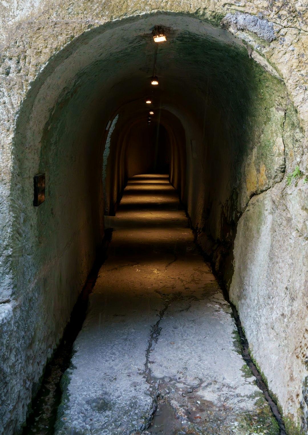 Ciemny kamienny tunel z łukowatym sklepieniem i oświetloną drogą.