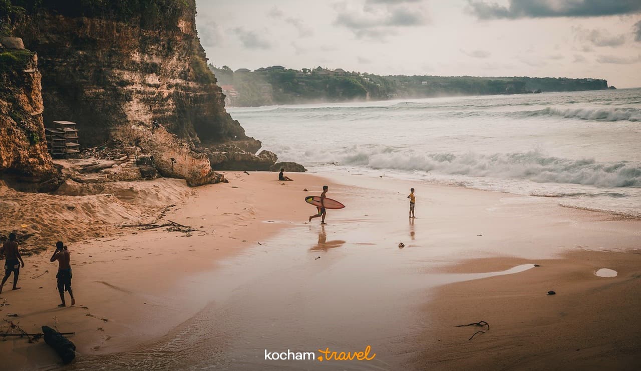 Piaszczysta plaża z surferami, klifami, dużymi falami oceanu.
