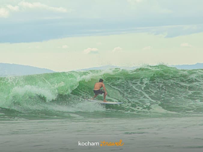 Surfer na dużej, zielonej fali z górami w tle