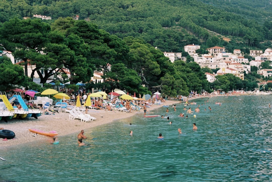 Tłoczna plaża z parasolami i pływającymi.