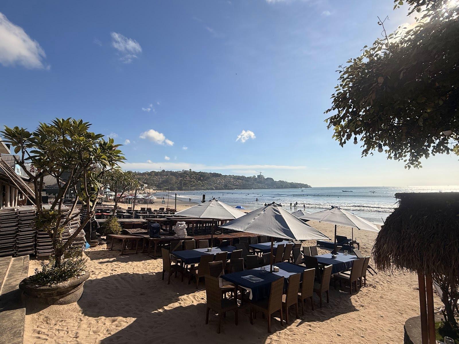 Słoneczna plaża z restauracją, parasolami i błękitnym oceanem.