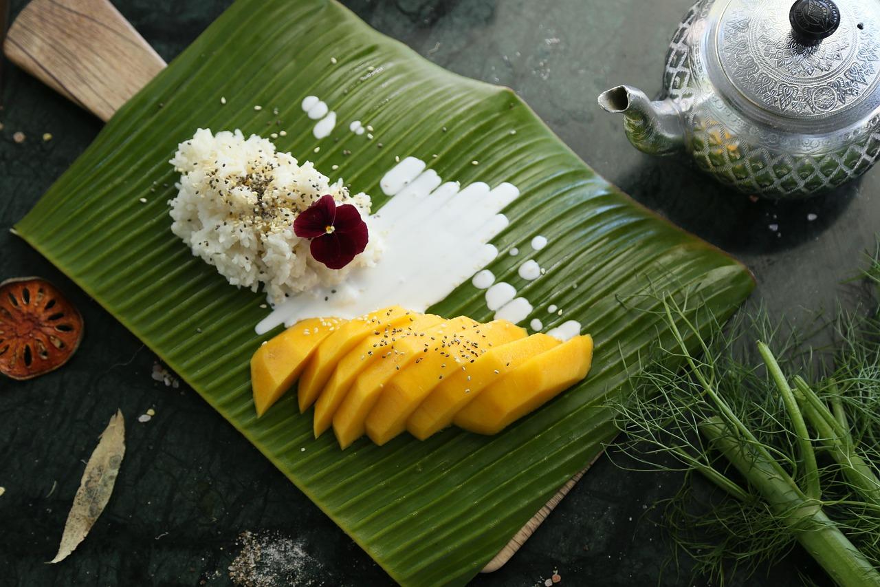 Egzotyczny deser mango sticky rice z sosem kokosowym i nasionami.