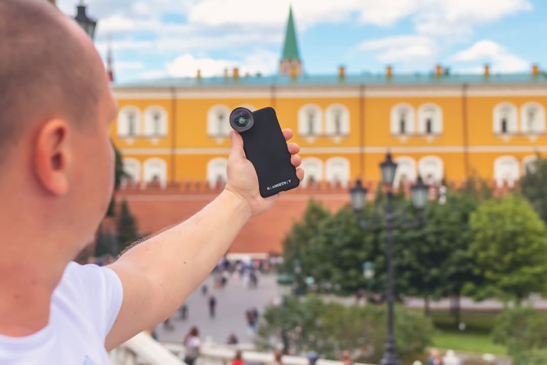 Osoba fotografuje zabytkowy budynek, używając smartfona z zewnętrznym obiektywem.