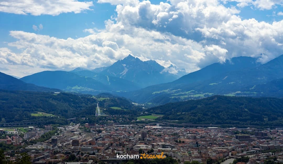 Panorama alpejskiego miasta w dolinie, otoczonego górami, ze skocznią narciarską.